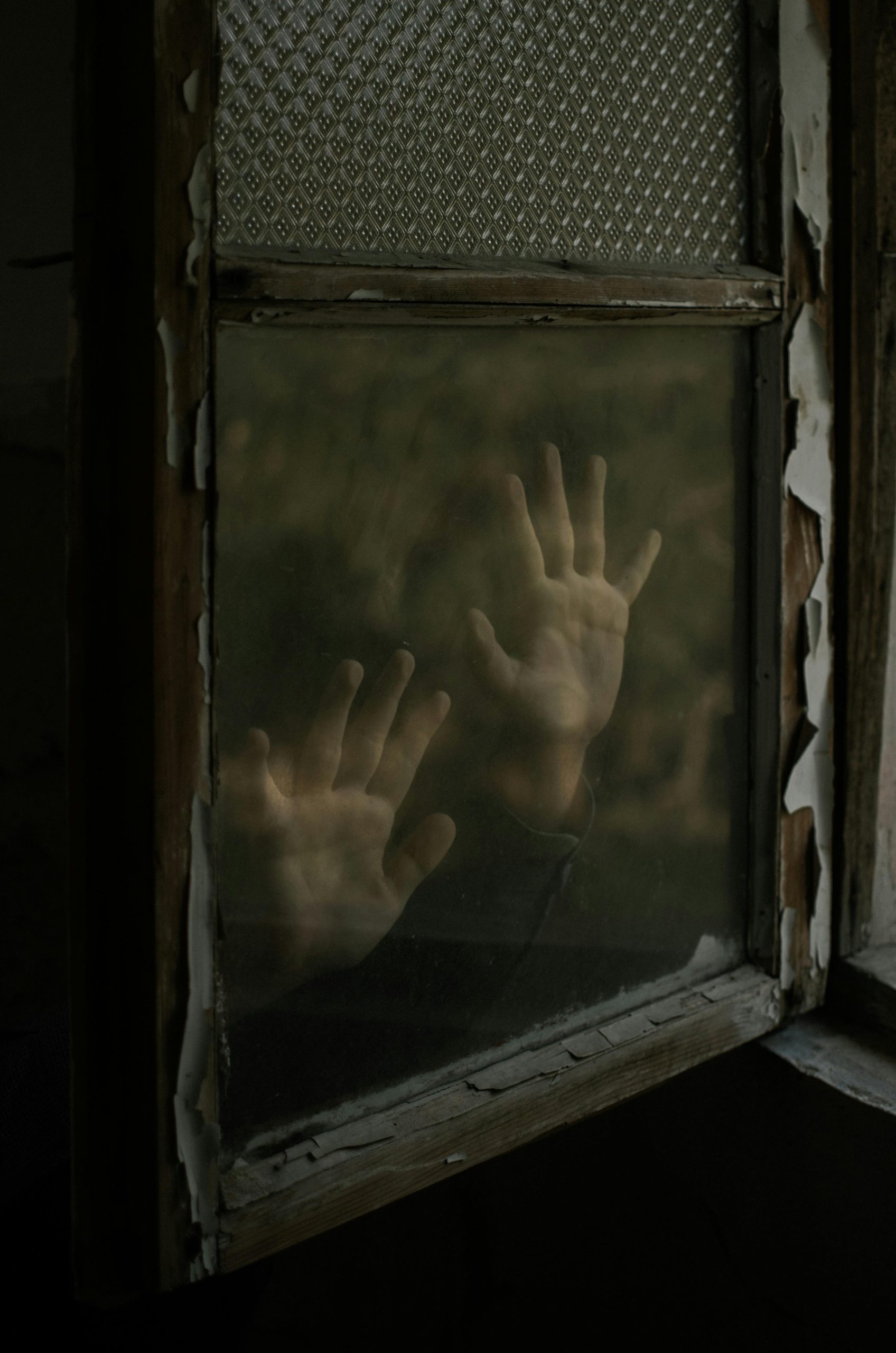 Mysterious hands pressed against an aged window, evoking isolation and entrapment.