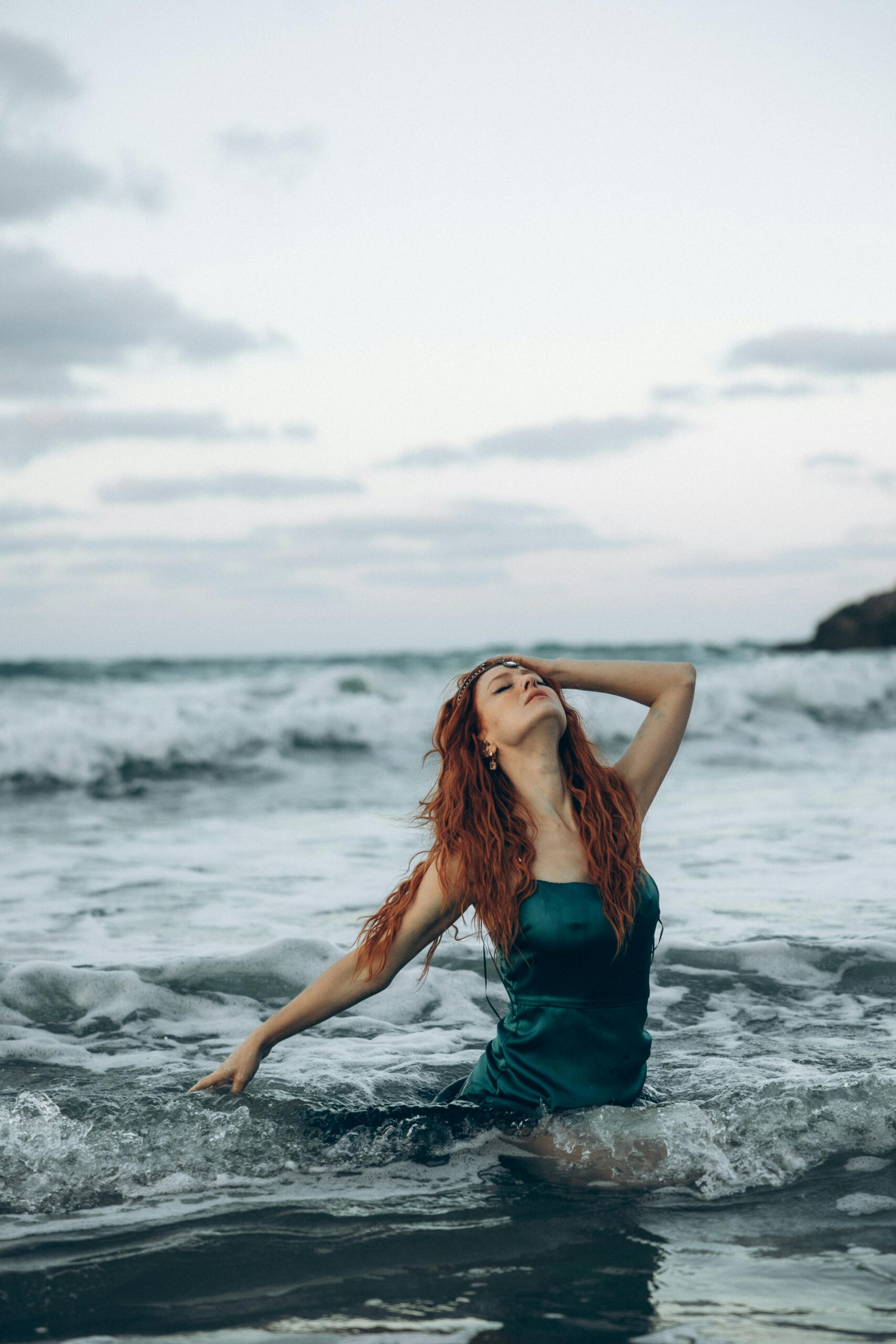 A woman with red hair gracefully enjoying the sea waves during sunset.