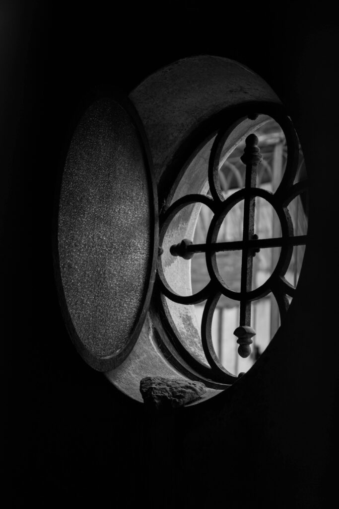 Black and white close-up of a round iron window with a unique pattern.